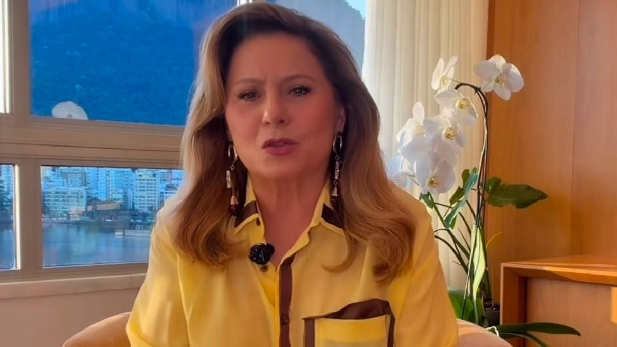 Vera Fischer em entrevista, refletindo sobre envelhecimento com expressão serena e direta, usando blusa amarela e falando em tom inspirador: “Não desapareci, continuo aqui”.