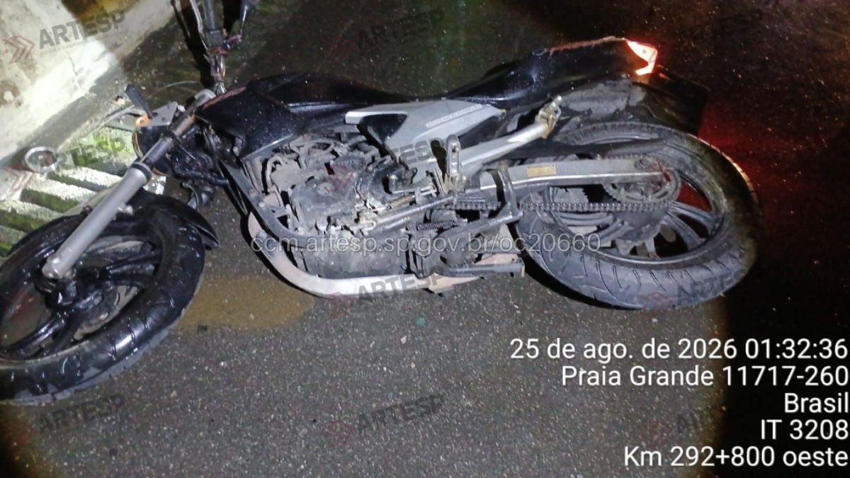 motociclista morre após bater contra barreira em Praia Grande: Motocicleta caída em via após acidente em Praia Grande, com motor e rodas visíveis no chão ao lado de barreira, em registro de reportagem.