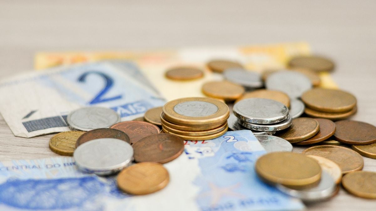 Moedas e cédulas sobrepostas em cenário econômico, com foco em economia brasileira; imagem que remete à queda de previsão do mercado para 2026 e às mudanças na estimativa.