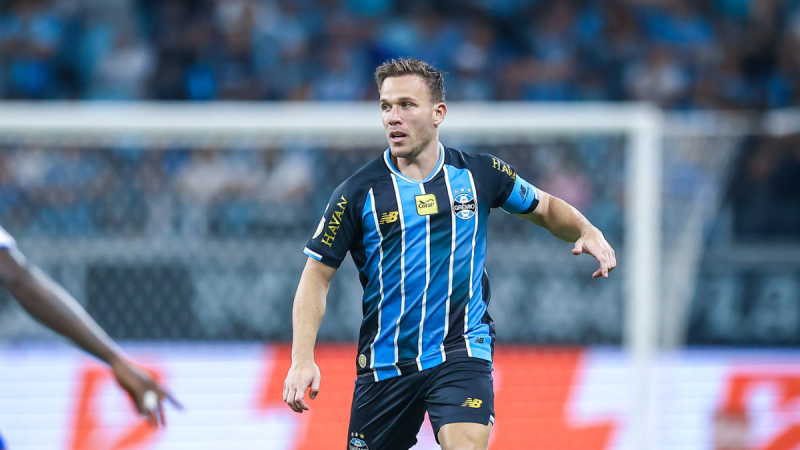 Arthur Melo em campo pelo Grêmio, durante partida com torcida ao fundo, em notícia sobre Santos tentando contratar Arthur Melo com ajuda de Neymar, ex-Barcelona.