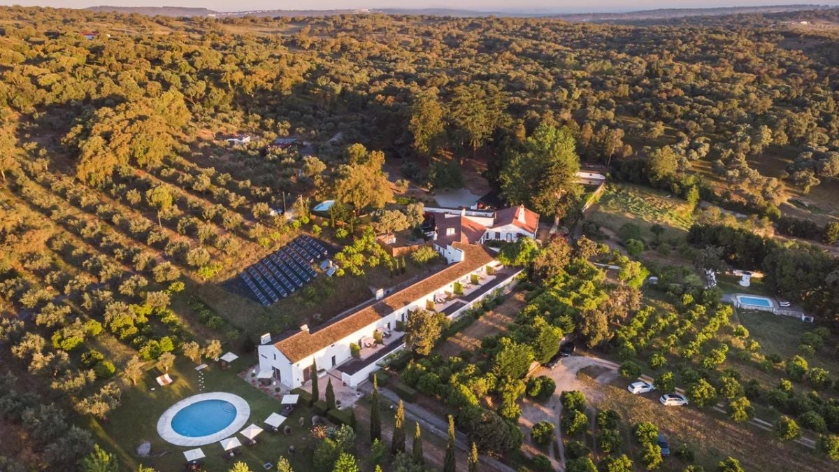 Aerial da Imani Country House no Alentejo, perto de Évora, cercada por campos e oliveiras, com casa de campo e piscina ao pôr do sol