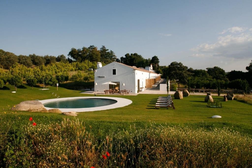 Imani Country House: refúgio de charme no Alentejo, perto de Évora, com casa branca, gramado verde e piscina ao ar livre em meio a jardins e árvores.