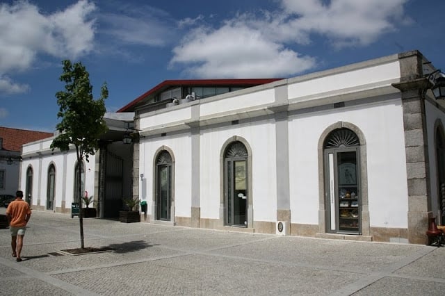 Imani Country House, refúgio de charme no Alentejo perto de Évora: fachada branca com arcos e janelas de vidro em um pátio com céu azul e nuvens