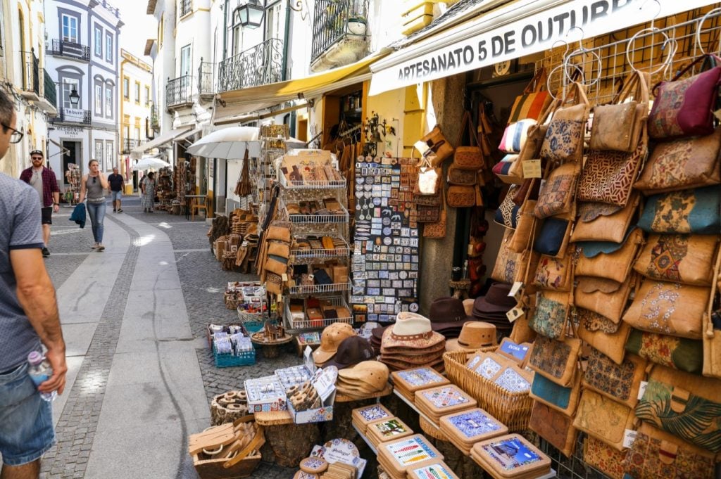 Loja de artesanato na rua, com bancas cheias de bolsas, carteiras e lembranças em couro e padrões coloridos, cenário do Alentejo perto de Évora: Imani Country House