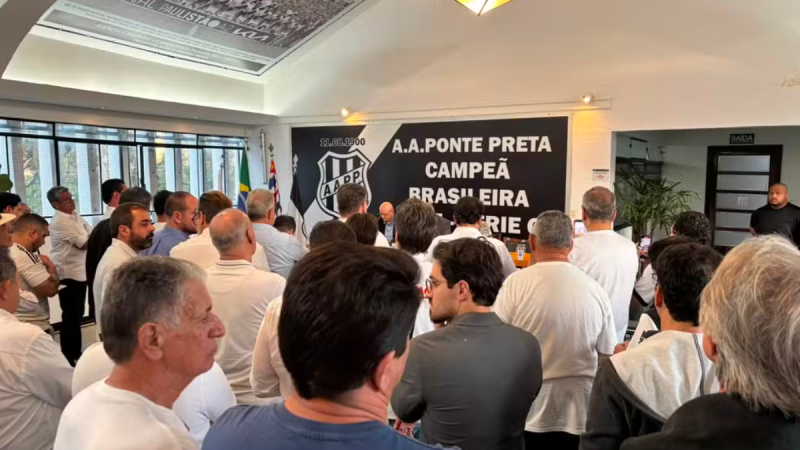 Pessoas em uma assembleia acompanham a votação sobre a Ponte SAF adiada após decisão da Justiça, em uma sala com bandeiras e telão com inscrições “A.A. PONTE PRETA”.