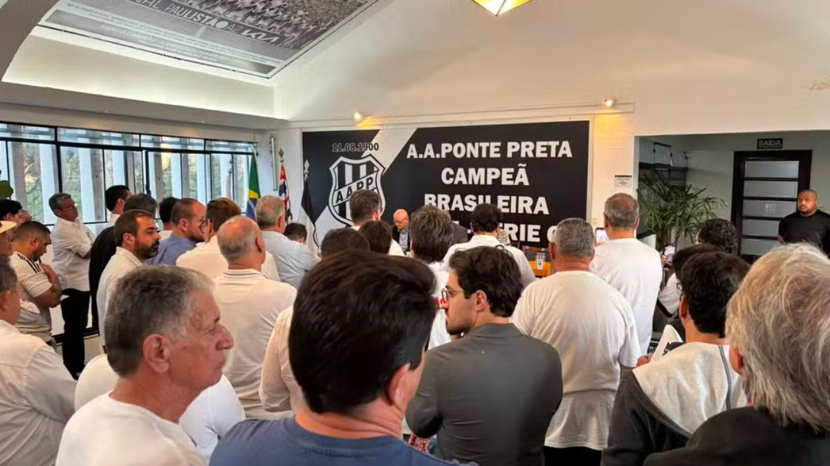 Pessoas em uma assembleia acompanham a votação sobre a Ponte SAF adiada após decisão da Justiça, em uma sala com bandeiras e telão com inscrições “A.A. PONTE PRETA”.