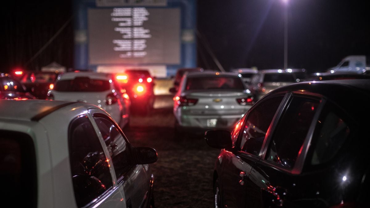 Cinema drive-in em Campinas à noite, com carros estacionados em fila para assistir a filmes em uma grande tela ao fundo