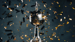 Imagem com uma taça de futebol em destaque, cercada por confetes dourados e pretos sobre fundo azul, representando a divulgação de Conmebol calendário para a temporada.