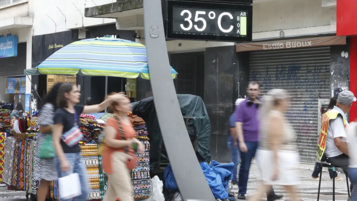 Mudanças bruscas de temperatura: pessoas circulam em rua comercial com painel digital marcando 35°C e variação térmica ao fundo, sugerindo “gangorra” climática em São Paulo