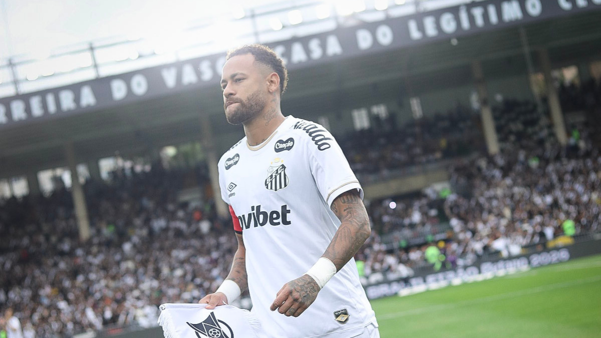 Neymar em estádio usando camisa do Santos, com expressão pensativa antes de partida; tema da imagem indica Neymar fora do clássico contra o Palmeiras e contra gramado sintético.