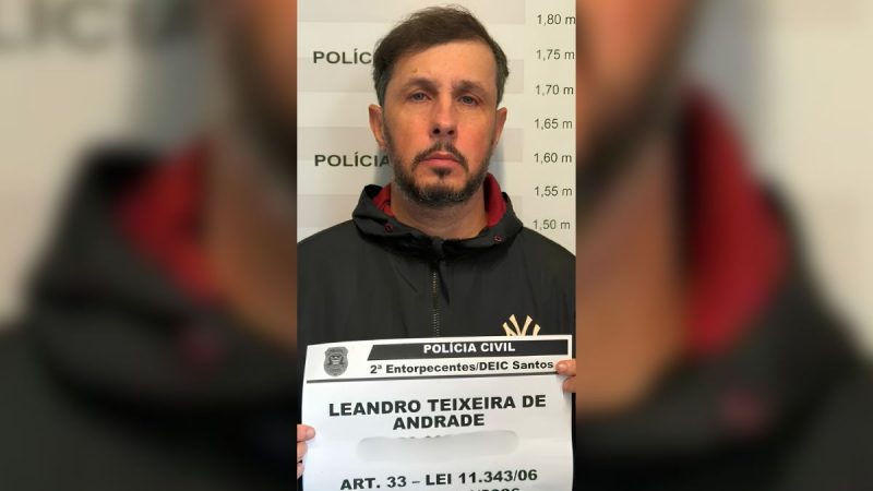 Homem ligado a André do Rap é preso: Homem identificado como Leandro Teixeira de Andrade é fotografado em apresentação da Polícia Civil, com placa de prisão e informações de Santos, ligado a André do Rap, em contexto de tráfico.