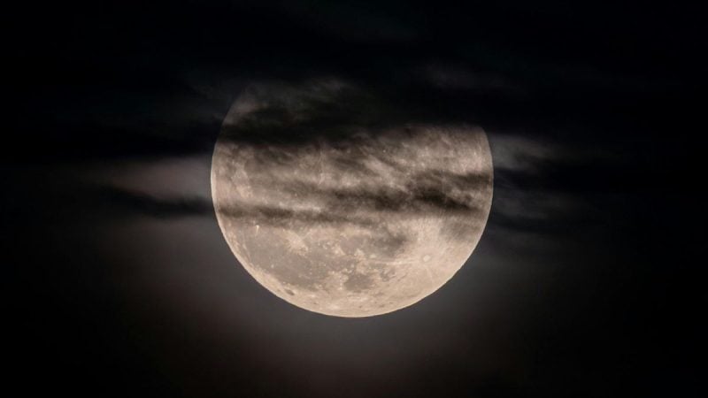 Eclipse lunar visível no céu, com a Lua parcialmente coberta e um tom avermelhado ao fundo, em uma cena noturna ideal para observar no Brasil.