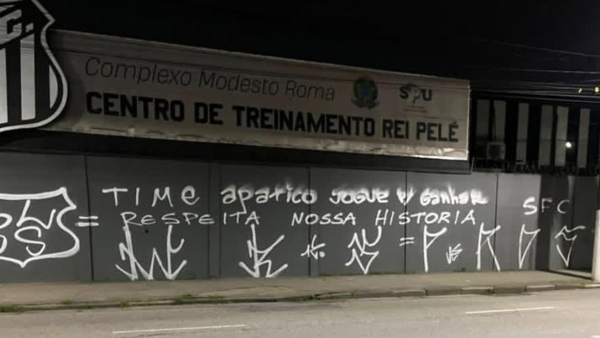 Muro do Centro de Treinamento Rei Pelé, do CT do Santos pichado após derrota, com frases e pichações em grafite à noite.