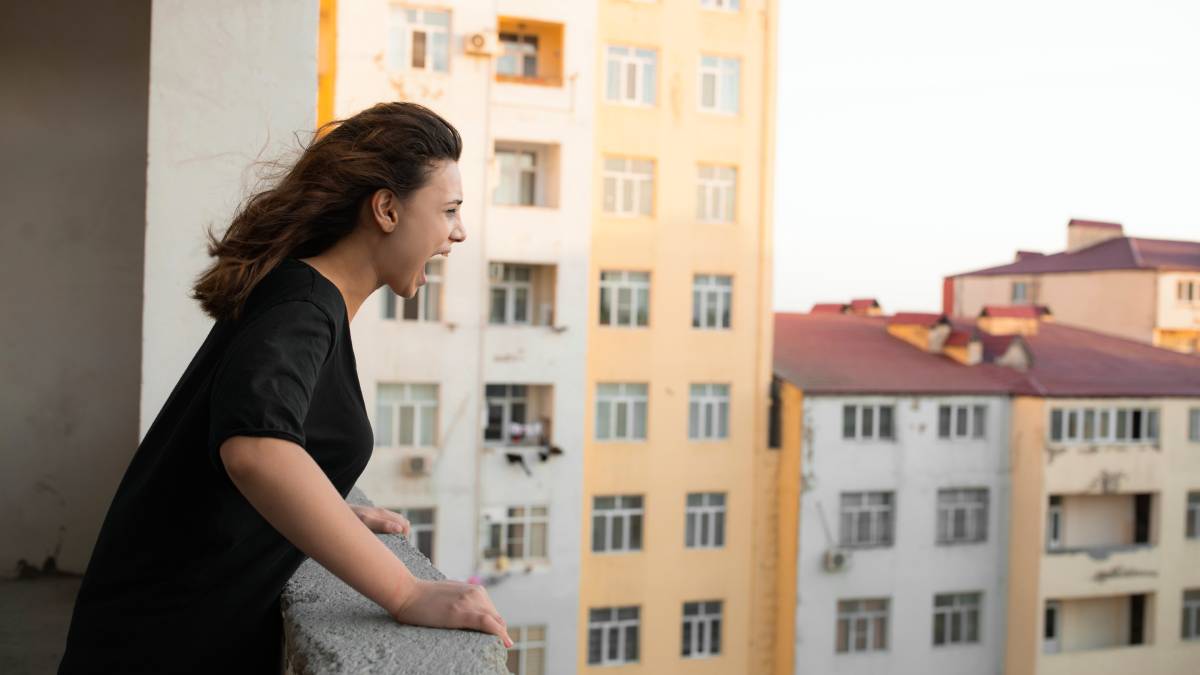 regras de condomínio: Mulher em varandas de um prédio de apartamentos observa o condomínio, em contexto de esclarecimentos do síndico sobre barulho e gás; foco em regras de convivência.