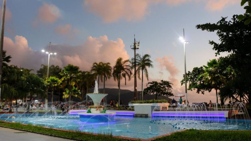 Chafariz iluminado em uma praça à noite, com palmeiras e céu com nuvens ao fundo; João Suplicy, Grease e Clássicos Encantados aparecem na agenda de Santos e destacam o que fazer em santos.
