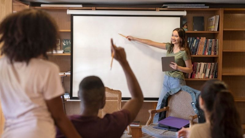 Atividades gratuitas senac: Aula prática em ambiente educacional, com instrutora utilizando quadro branco e alunos sentados em sala de aula, participando de uma atividade orientada.