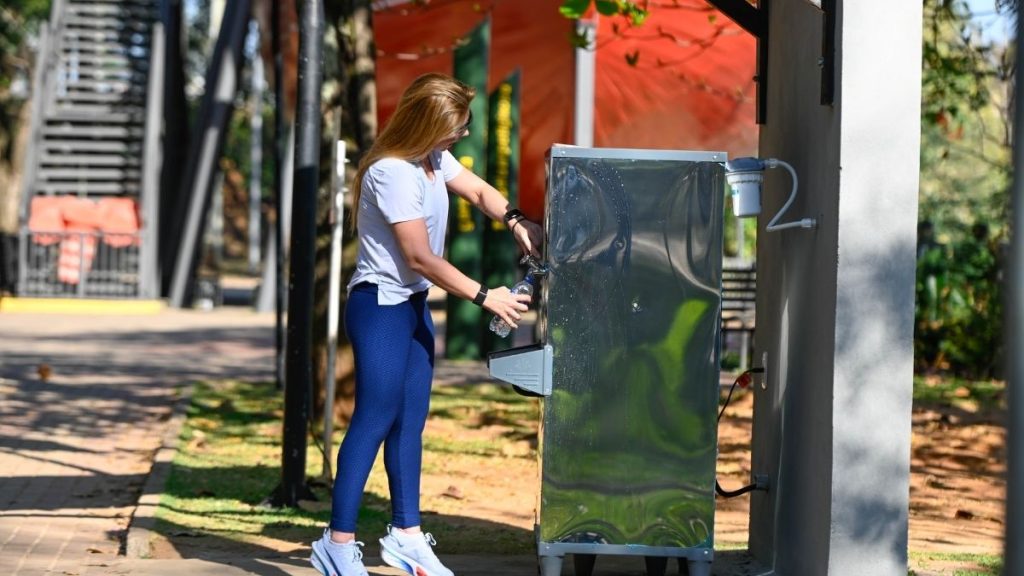 Pessoa usando uma máquina de serviço ao ar livre em um ambiente comercial, com estrutura metálica e painel elétrico, em dia ensolarado