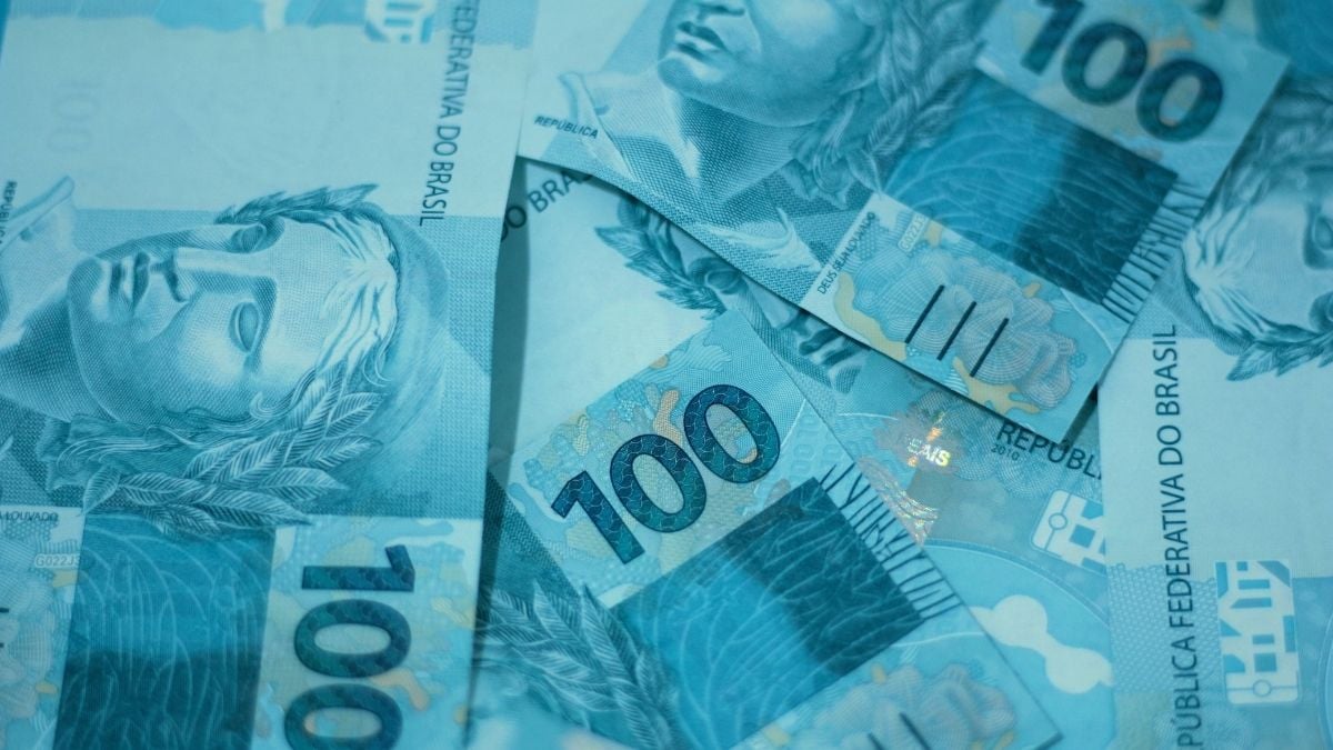 10 maiores bilionários do Brasil — Forbes divulga o ranking com uma imagem de cédulas de dinheiro brasileiro em tom azul, destacando notas de 100 reais e 10 reais ao fundo.