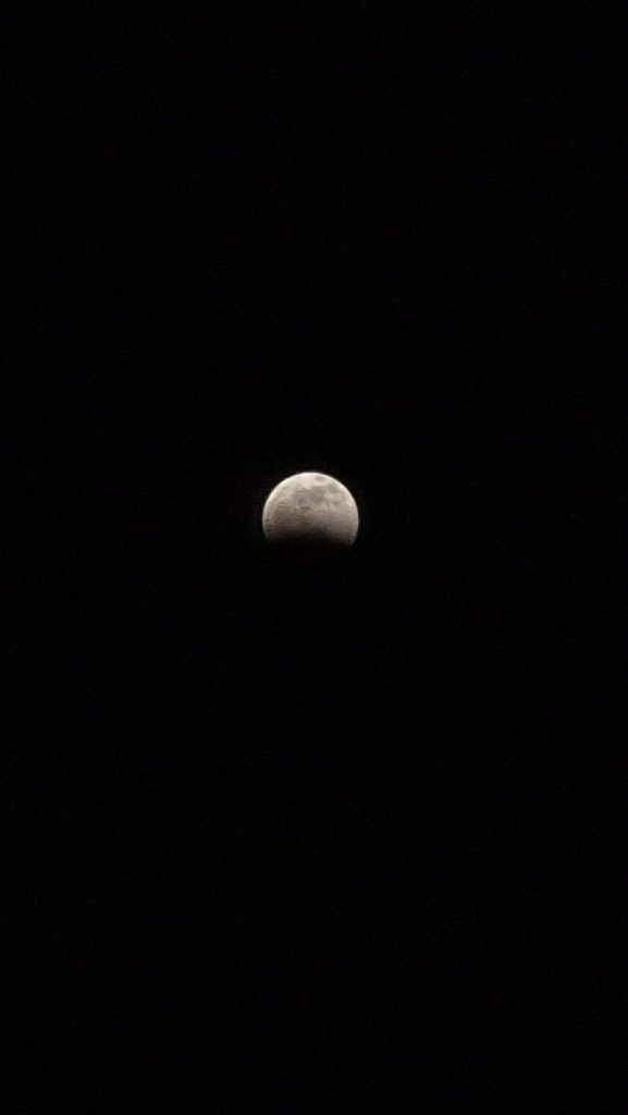 Lua parcialmente iluminada vista contra um fundo escuro, com aparência granular e detalhes sutis de sombras no disco lunar.