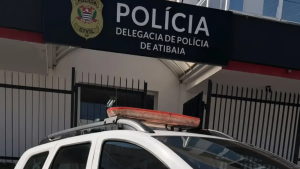 Homem preso por violência doméstica em Atibaia após agredir a mãe e a irmã, com viatura da Polícia Civil e fachada da Delegacia de Polícia de Atibaia ao fundo