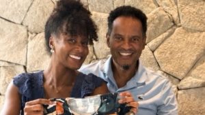 gravidez Maju Coutinho: Maju Coutinho anuncia gravidez e revela nome do filho ao lado do marido, em foto sorridente com ambos sentados em ambiente externo e iluminação natural.