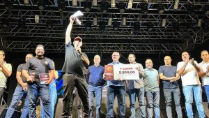 Vencedores do Concurso gastronômico de Americana de 2025, em foto de premiação no palco, com troféu/placa e valores exibidos enquanto o vencedor ergue o prêmio ao microfone.