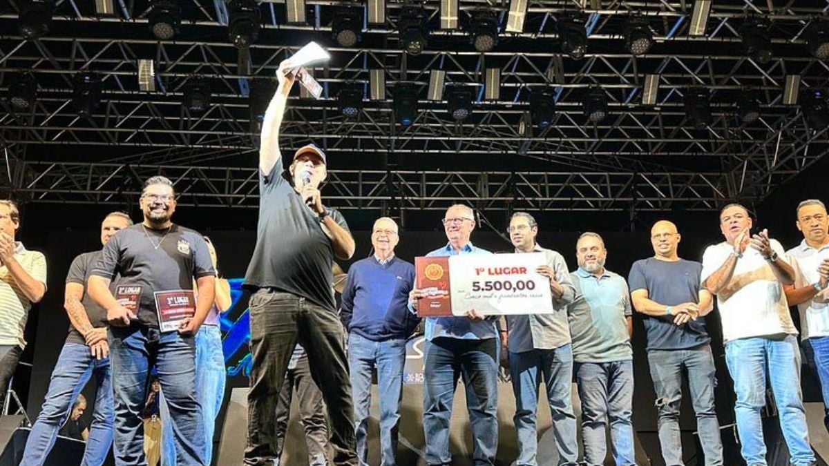 Vencedores do Concurso gastronômico de Americana de 2025, em foto de premiação no palco, com troféu/placa e valores exibidos enquanto o vencedor ergue o prêmio ao microfone.