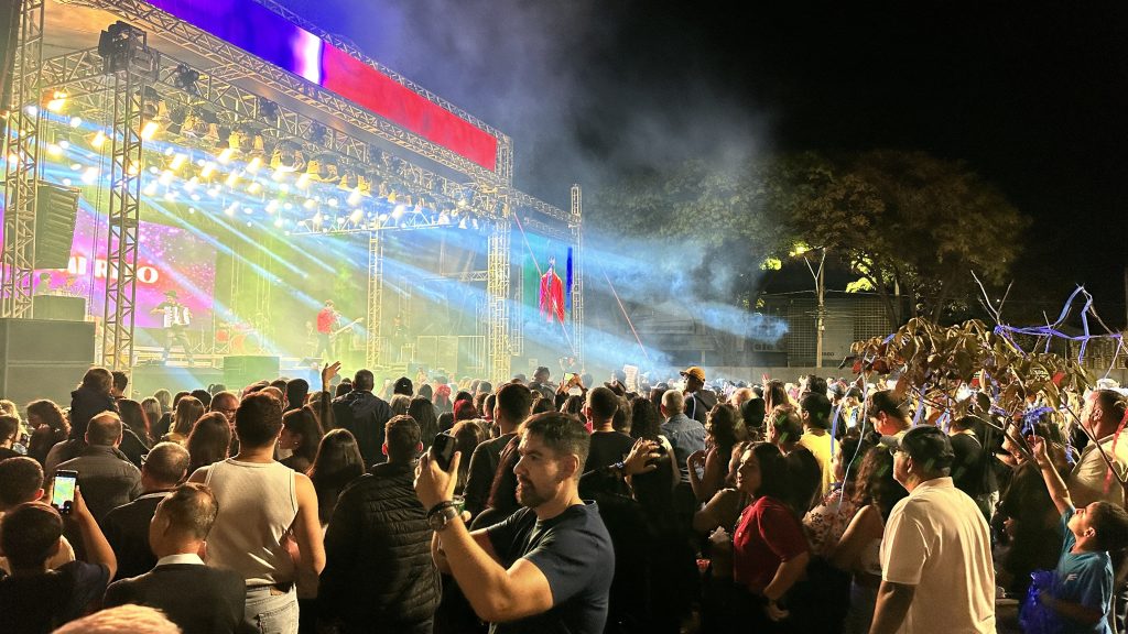 Centenas de pessoas assistem ao show do Roteiro Gastronômico de Americana em frente ao palco iluminado, com fumaça e luzes coloridas à noite.