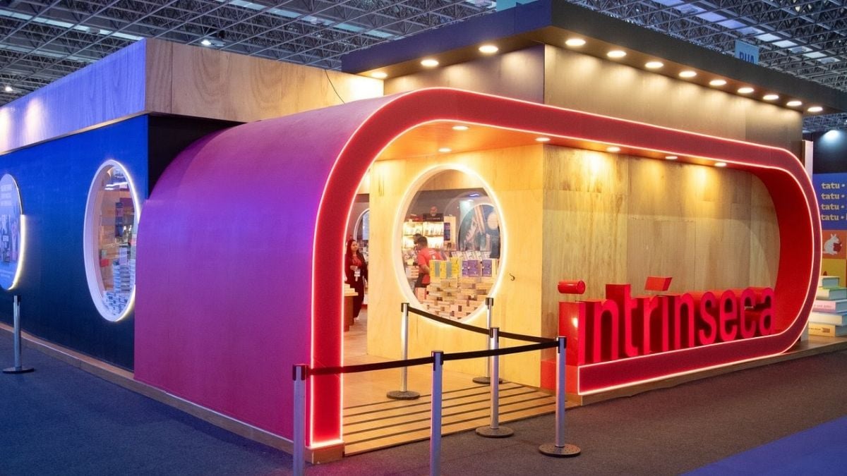 Bienal do Livro de SP 2026: estande com estrutura iluminada em tons de vermelho e amarelo em feira de livros, com área de visita ao fundo