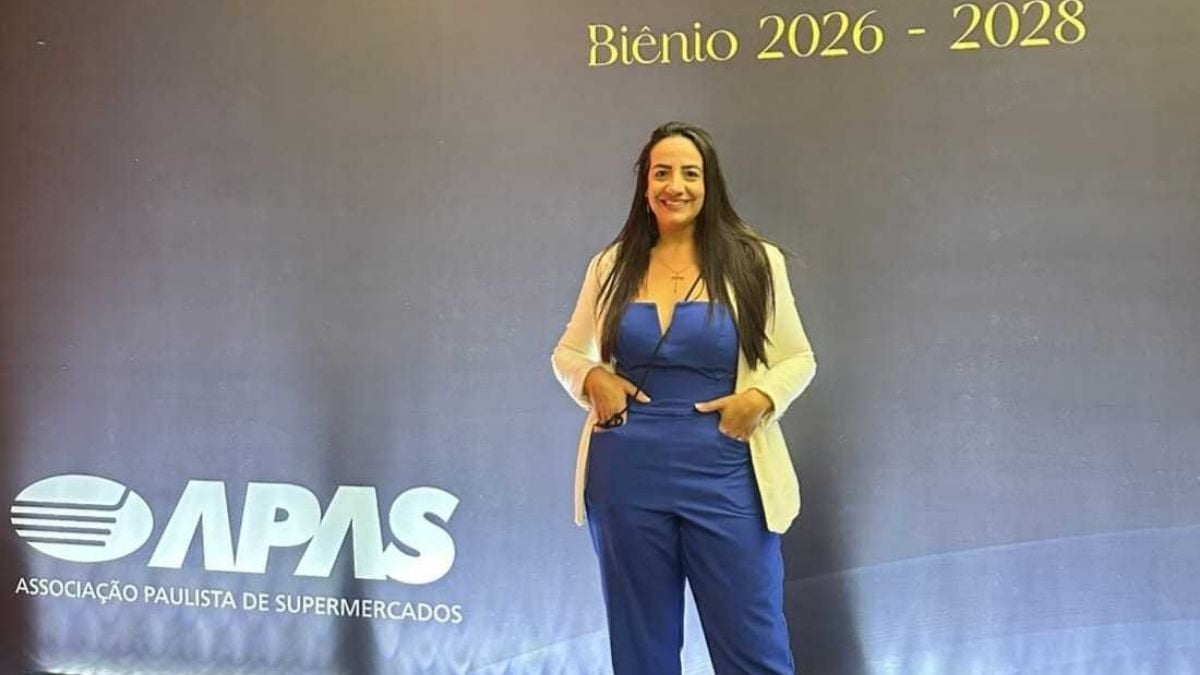 Imagem promocional com a frase “CERIMÔNIA DE POSSE” e a indicação “Biênio 2026 - 2028”, ao lado do logotipo APAS (Associação Paulista de Supermercados). Há uma mulher em pé, sorrindo, no palco com roupa azul e blazer branco.