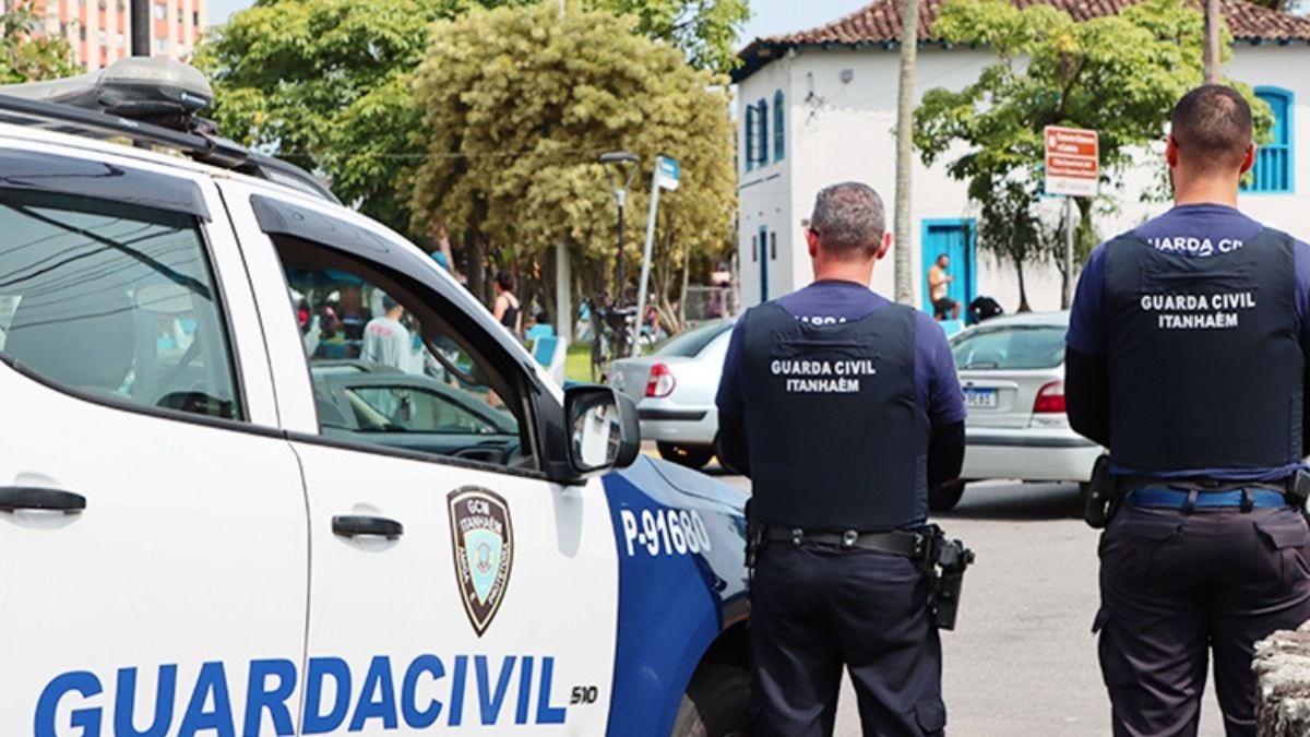 Agentes da Guarda Civil estão em patrulhamento na rua, próximos a viaturas e veículos estacionados, com uniforme “Guarda Civil” e identificação “Guarda Civil Itanhaém”.