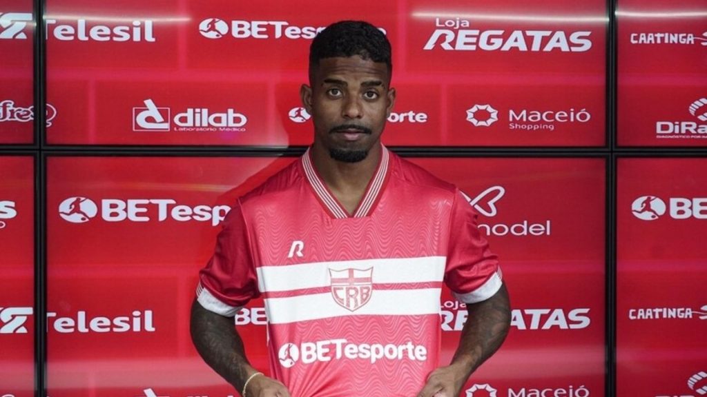 Hayner em foto de apresentação diante de um painel vermelho de patrocínios, vestindo o uniforme do Santos e em referência ao empréstimo ao Vila Nova