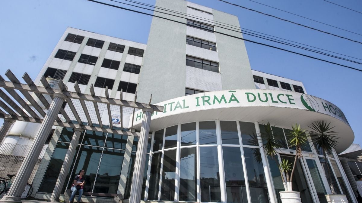 menina cai de prédio em Praia Grande: Prédio em Praia Grande com fachada e nome “ITAL IRMÃ DULCE”, visto da rua, com grades e fios elétricos na frente, em notícia sobre queda de criança.