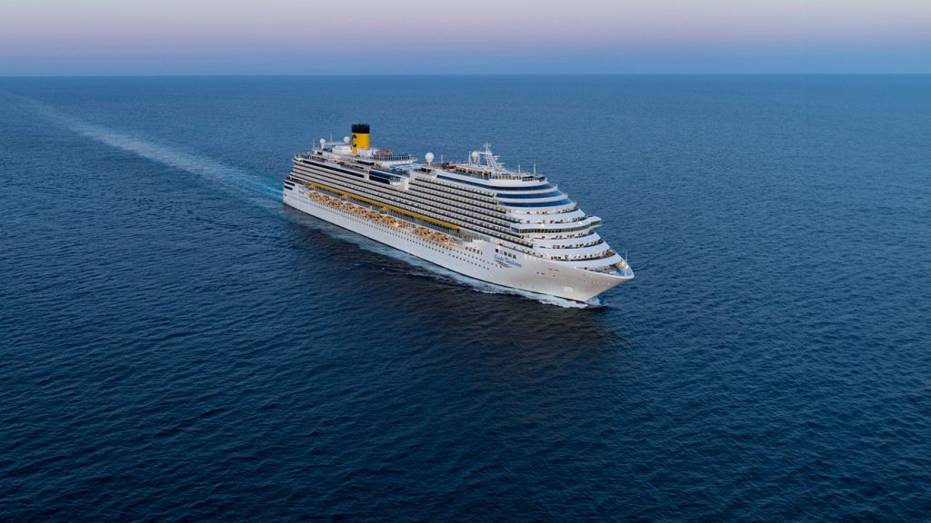temporada de cruzeiros 2026/2027: Costa Diadema navegando em alto-mar, com o navio de cruzeiro branco ao centro cortando as águas azuis ao amanhecer, visto de cima