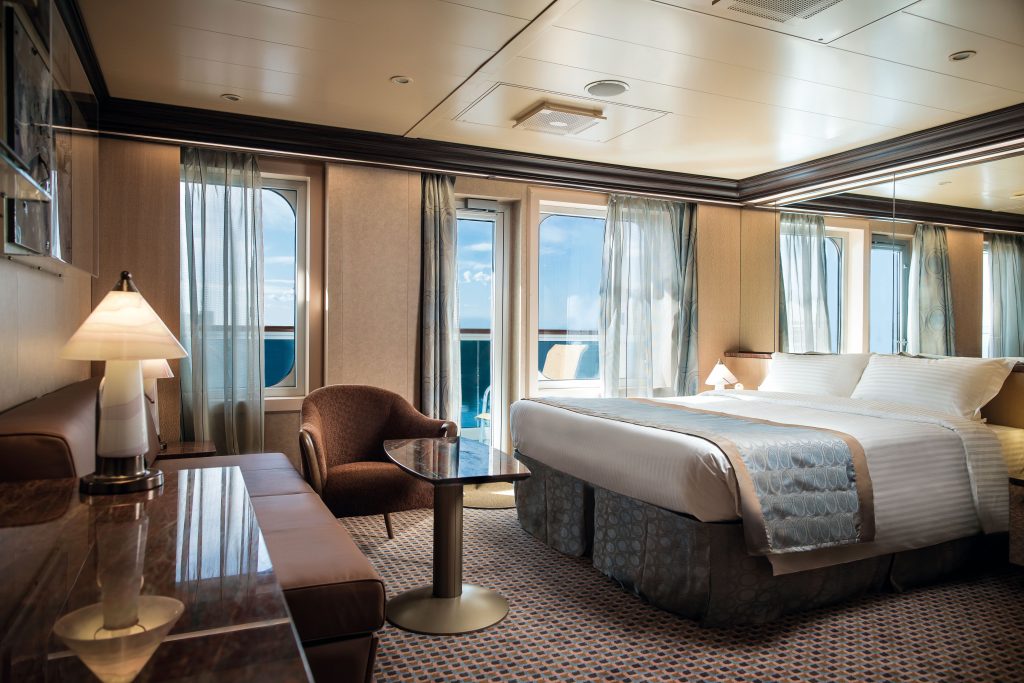 Interior de cabine em estilo moderno com cama de casal, poltrona e janelas amplas com vista para o mar a bordo do navio Costa Diadema, ideal para temporada de cruzeiros 2026/2027.