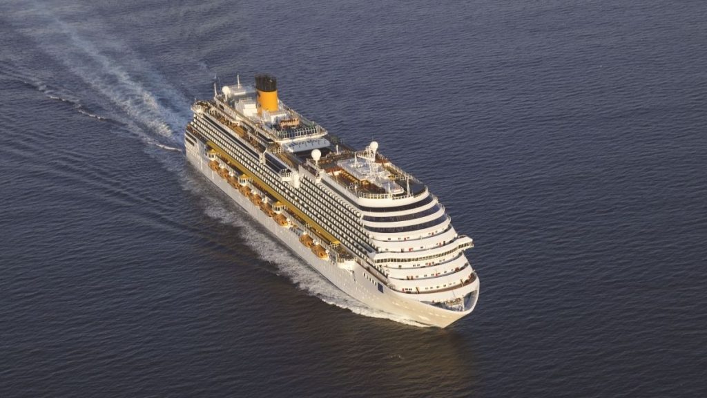 temporada de cruzeiros 2026/2027: Costa Diadema, navio de cruzeiro da Costa, navegando sobre as águas do mar em imagem aérea, com rastro de espuma atrás e destaque para o casco e bandeiras