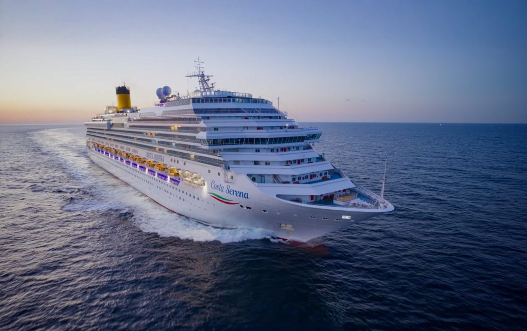 Costa Serena, navio de cruzeiro da Costa, navegando pelo mar ao pôr do sol, com luzes noturnas e rota ao horizonte, ideal para temporada de cruzeiros 2026/2027