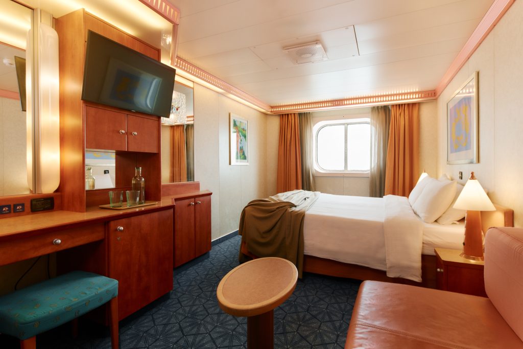 temporada de cruzeiros 2026/2027: Interior de cabine de cruzeiro Costa Serena com cama, mesa lateral, poltrona, armário e janela para o mar.