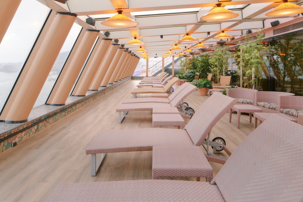 Área externa do navio Costa Serena com espreguiçadeiras, mesas e ambiente interno com iluminação, ideal para relaxar durante a temporada de cruzeiros 2026/2027
