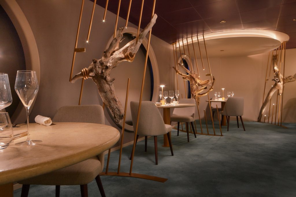 Mesa posta e decoração sofisticada no interior do navio Costa Serena, com cadeiras, taças e luzes ao fundo para uma experiência de temporada de cruzeiros 2026/2027.