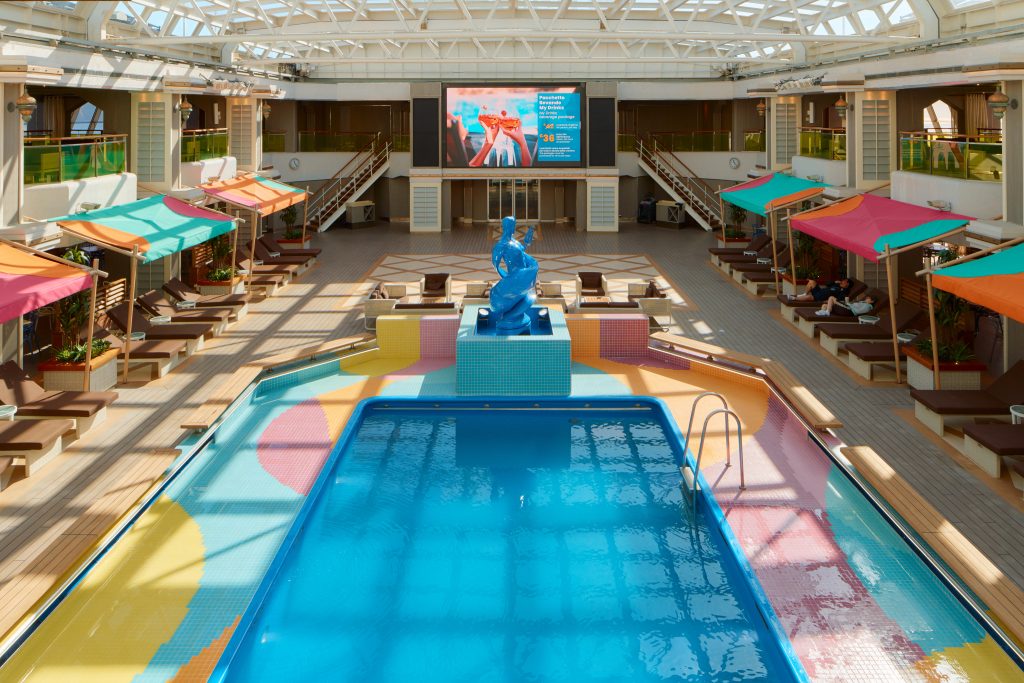 Área de piscina do navio Costa Serena com espreguiçadeiras coloridas, ambiente externo iluminado pelo sol e estrutura coberta no deck, ideal para temporada de cruzeiros 2026/2027.