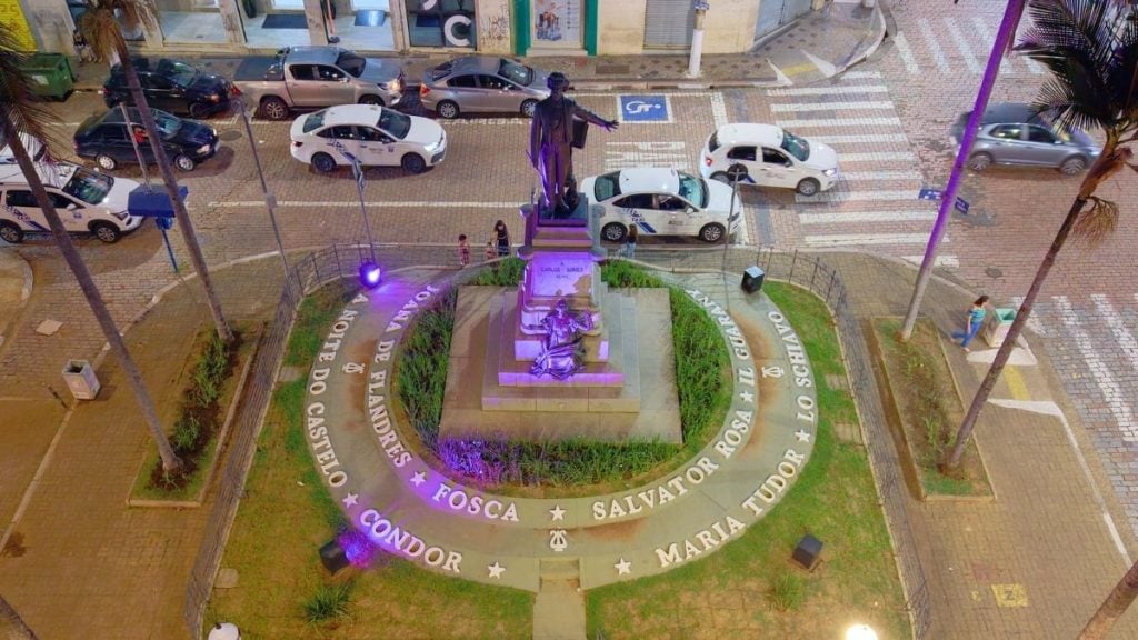 Estátua Carlos Gomes Campinas em pedestal no centro do memorial, com jardim ao redor e iluminação roxa remetengo a programação gratuita em setembro.