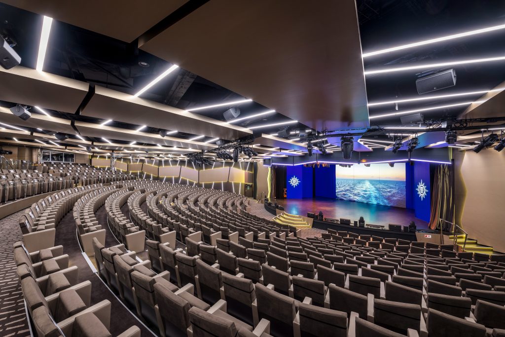 Interior do teatro do navio MSC Virtuosa, com fileiras de assentos e palco iluminado no estilo Minuetto, cenário para apresentações durante a temporada de cruzeiros 2026/2027.
