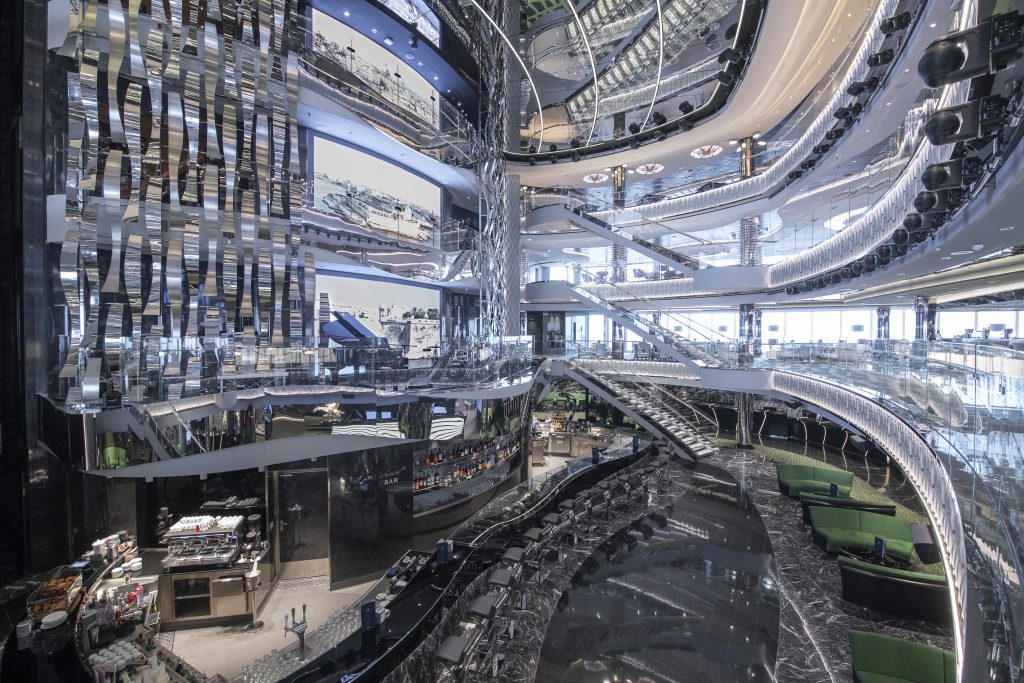 temporada de cruzeiros 2026/2027: Atrium do navio MSC Seaview, com vista para os andares internos, estruturas curvas modernas, áreas de estar e iluminação em tons azulados e prateados
