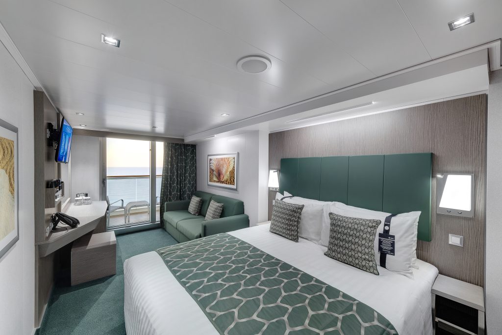 temporada de cruzeiros 2026/2027: Quarto no navio MSC Seaview com cama de casal, headboard verde, edredom e almofadas, além de varanda Deluxe Balcony (BR3) visível ao fundo, com janelas amplas e área de estar.