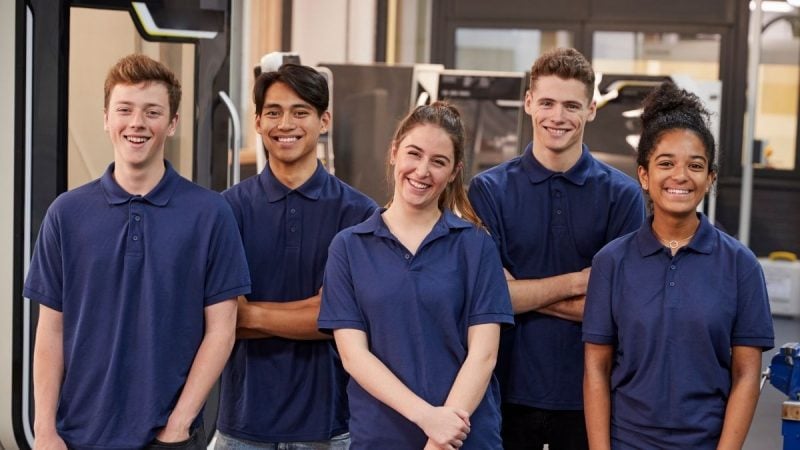Grupo de jovens sorrindo em ambiente profissional, com uniformes, fazendo referência ao Programa Aprendiz Sabesp.
