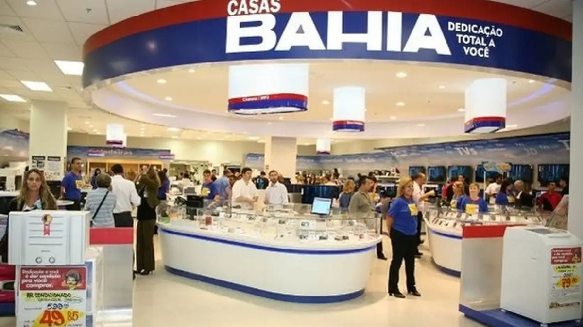 Lojas Casas Bahia com balcões de atendimento e banner “Casas Bahia”, em ambiente de shopping com vendedores e clientes ao fundo, sugerindo leilão de eletrônicos e eletrodomésticos.
