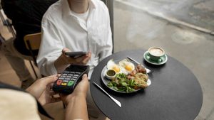 Abrasel abre inscrições para evento de gestão de bares, com cena de pagamento por cartão e mesa com prato e café em ambiente gastronômico, sugerindo como participar.