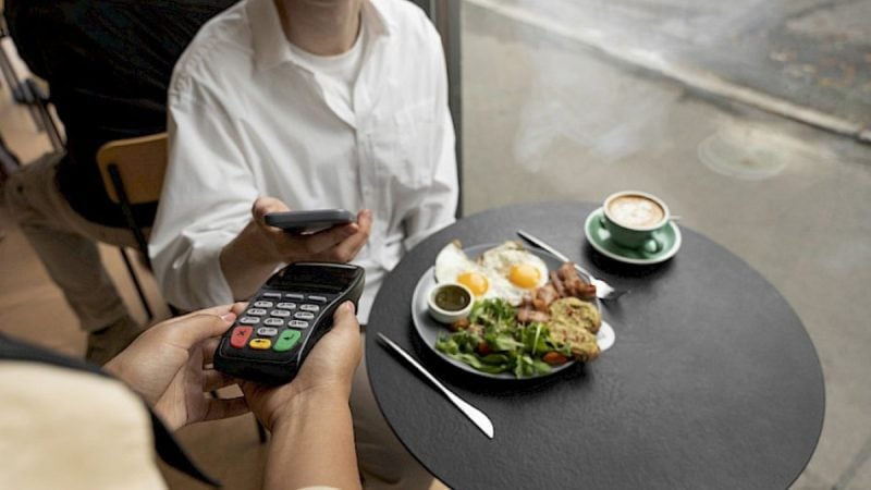 Abrasel abre inscrições para evento de gestão de bares, com cena de pagamento por cartão e mesa com prato e café em ambiente gastronômico, sugerindo como participar.