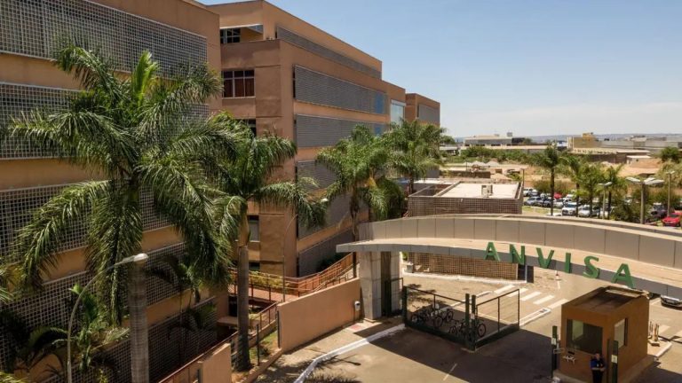 Prédio da Anvisa com a fachada “ANVISA” em destaque, visto em ambiente externo com jardins e estacionamento, relacionado à notícia sobre suspensão da fabricação da Unilever em Vinhedo.